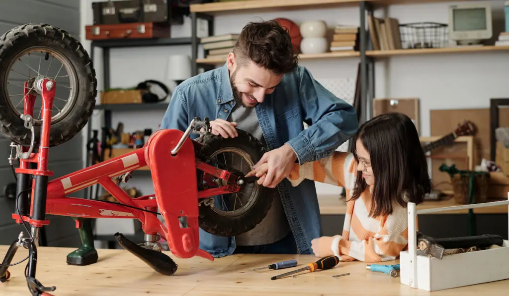young man and his daughter fixing a bike on a workbench