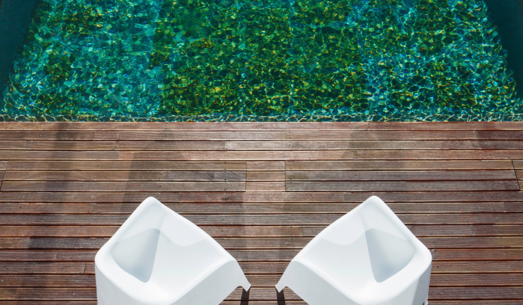 two white plastic chairs on the wooden deck and a pool