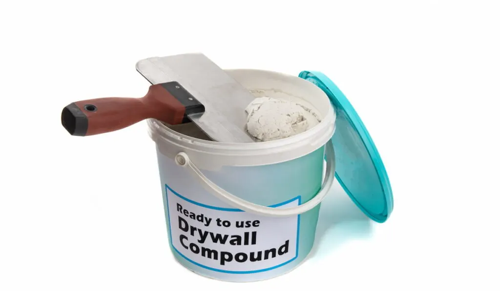 An open plastic pail of drywall joint compound, with a generic fake label with a wide drywall joint knife on white background