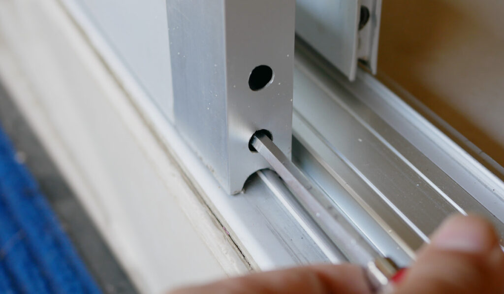 Close up of a screwdriver in a man's hand adjusting sliding glass door rollers