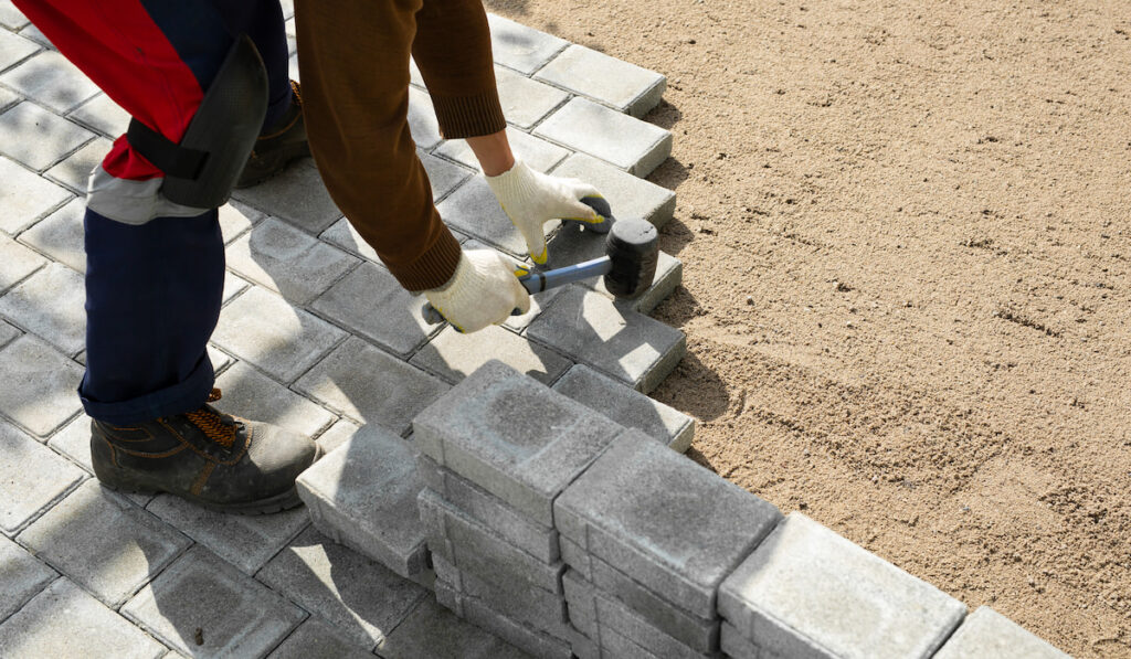Hands of a worker installing concrete blocks, paving slabs with a rubber hammer 