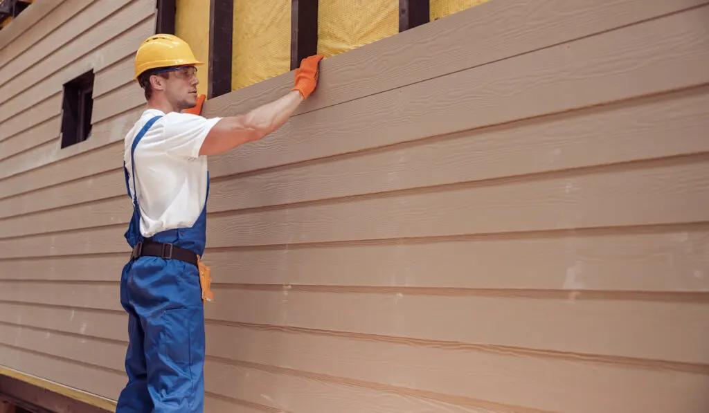 Male worker building house siding at construction site
