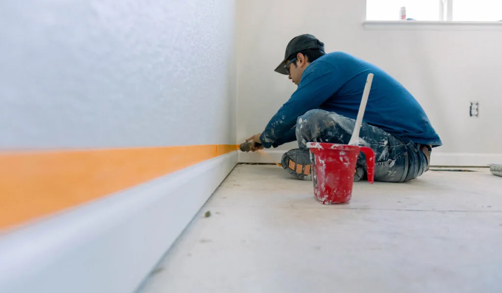 Man taping the wall to paint the trim white on a home renovation project 