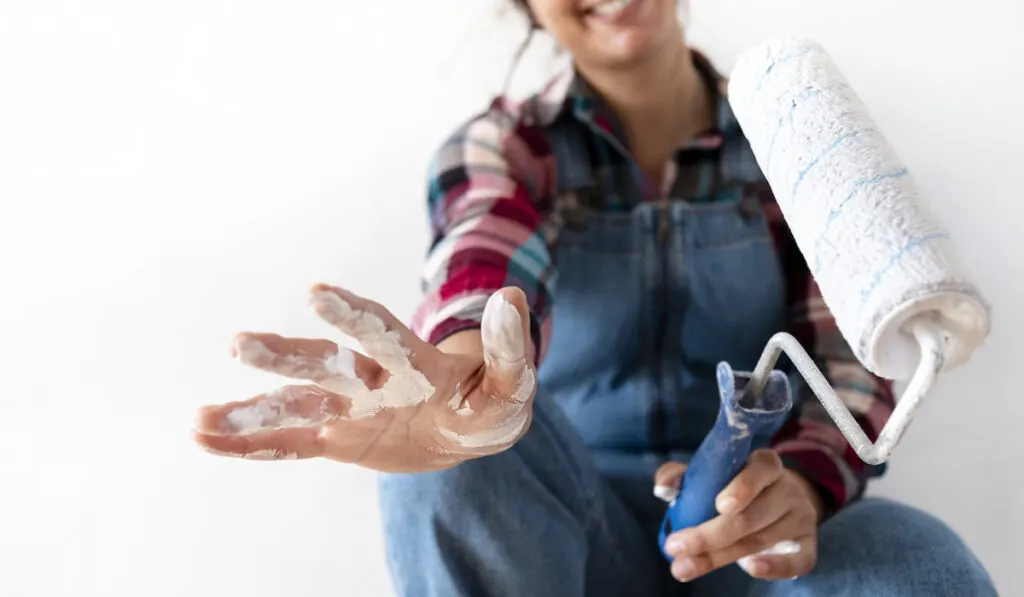Young woman showing hand with paint. Holding a paint roller