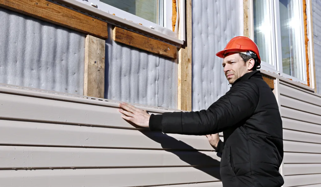 man installs panels beige siding on the facade of the house