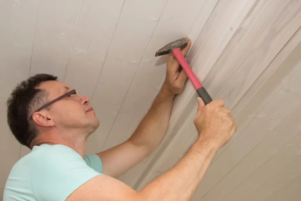 man nailing a nail back into the ceiling