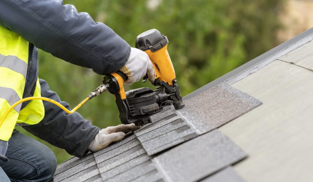 roofer installing asphalt or bitumen tile on top of the roof under construction house