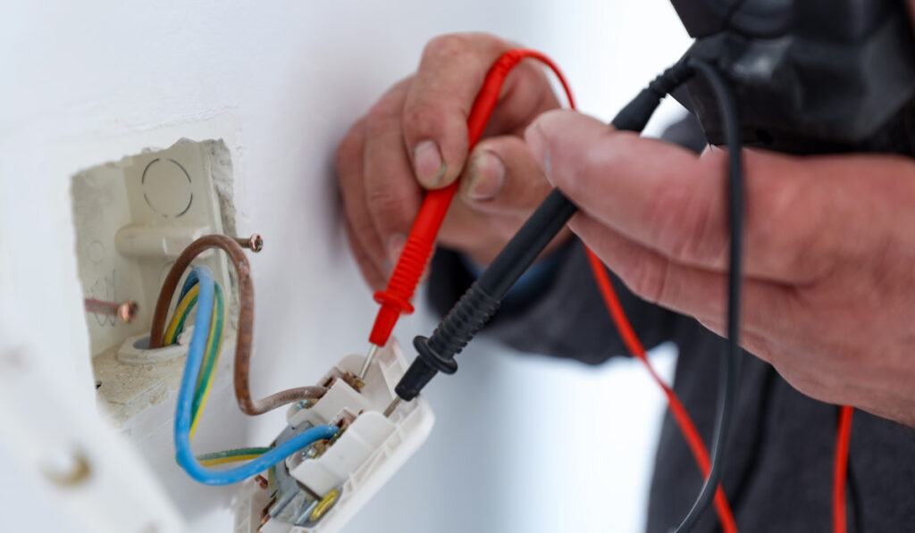 An electrician using a multimeter to check voltage in a domestic socket outlet