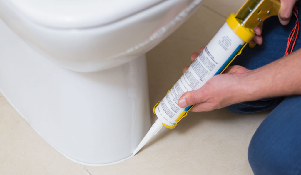 Close up of a plumber fixing toilet in a washroom with silicone