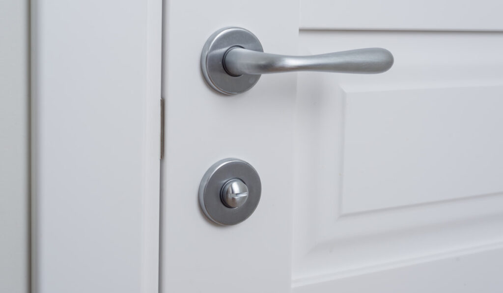Detail of a white interior door with a chrome door handle and latch 