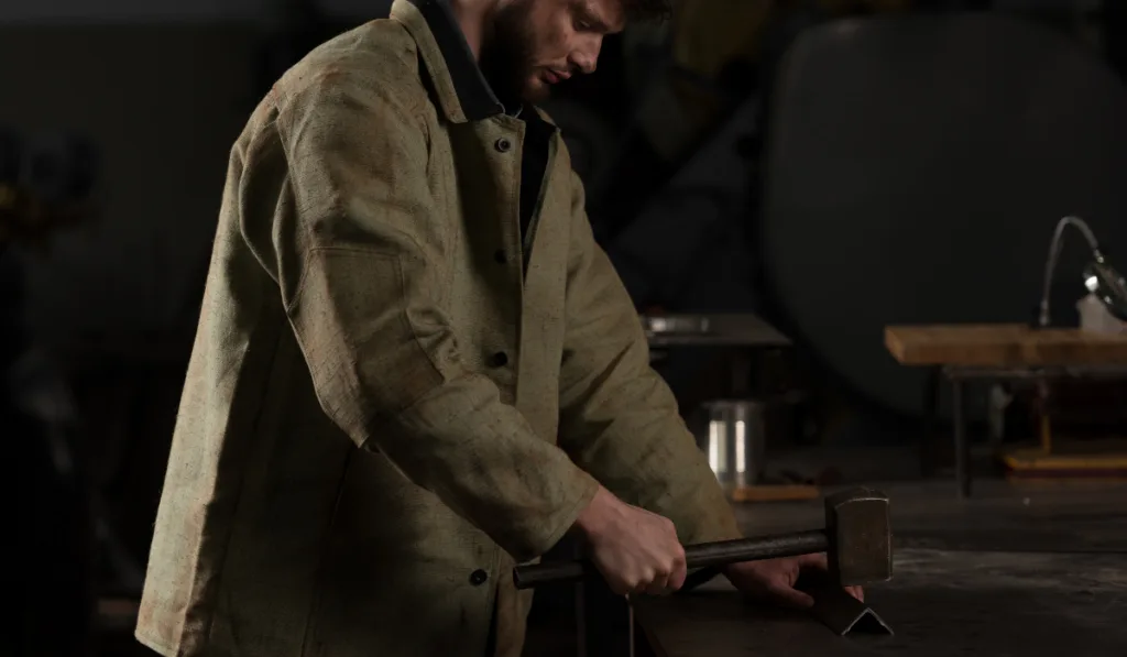 Young Workman With Hammer And Metal Part at Factory