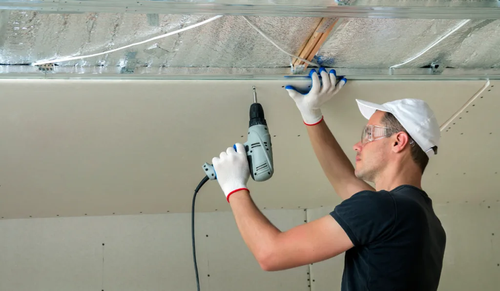 Young man in goggles fixing drywall suspended ceiling 