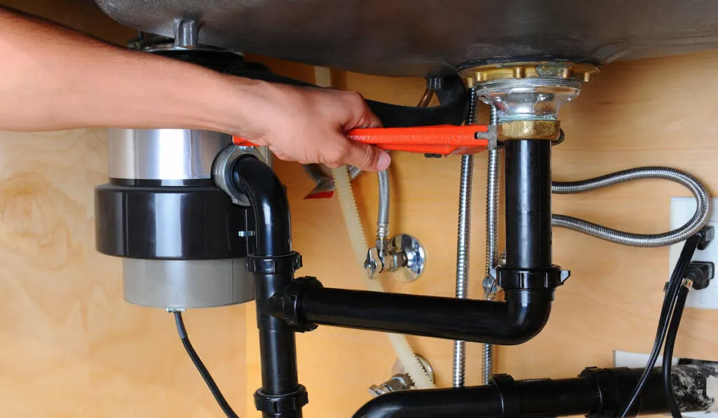 Closeup of a plumber using a wrench to tighten a fitting beneath a kitchen sink and garbage disposal