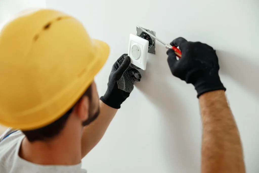 Professional electrician in uniform using screwdriver while installing electrical socket outlet
