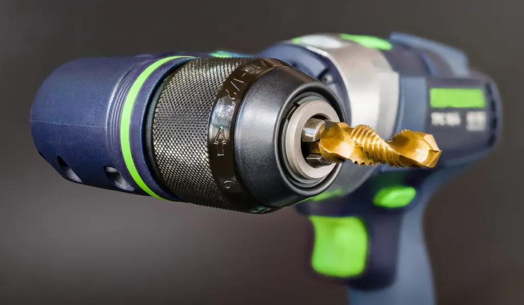 Steel tap and drill bit in power screwdriver right angle head on a gray background 