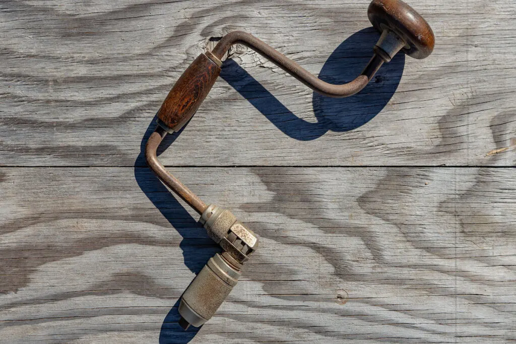 Vintage brace and bit drill on weathered wood background
