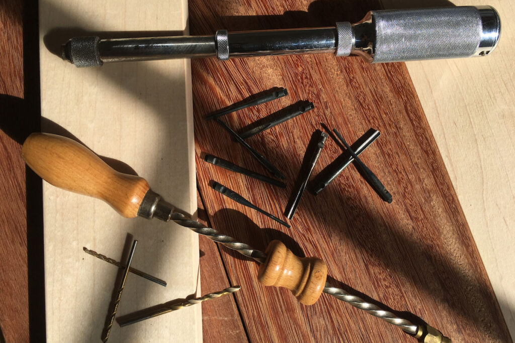 Vintage hand push drill and Archimedes drills and bits over maple and sapele boards.