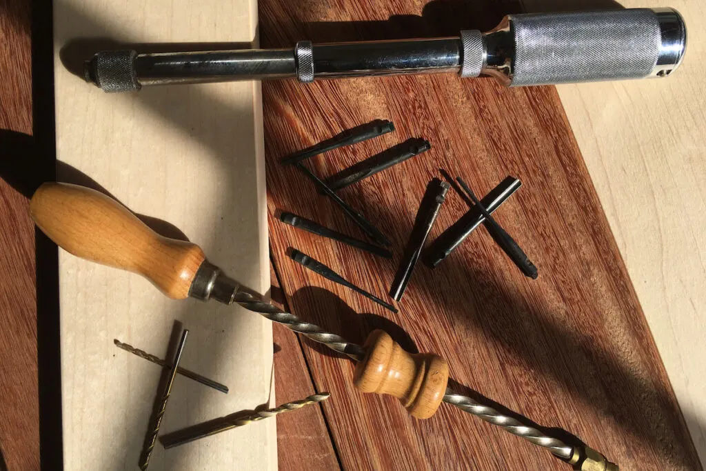 Vintage hand push drill and Archimedes drills and bits over maple and sapele boards.