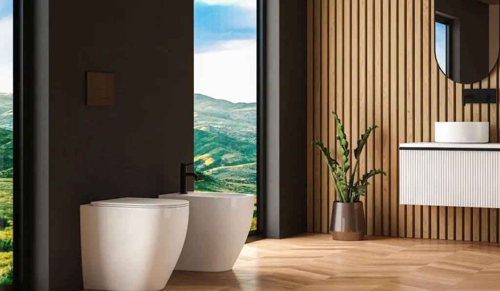 back to wall toilet and bidet on parquet floor in modern bathroom with black and wooden walls