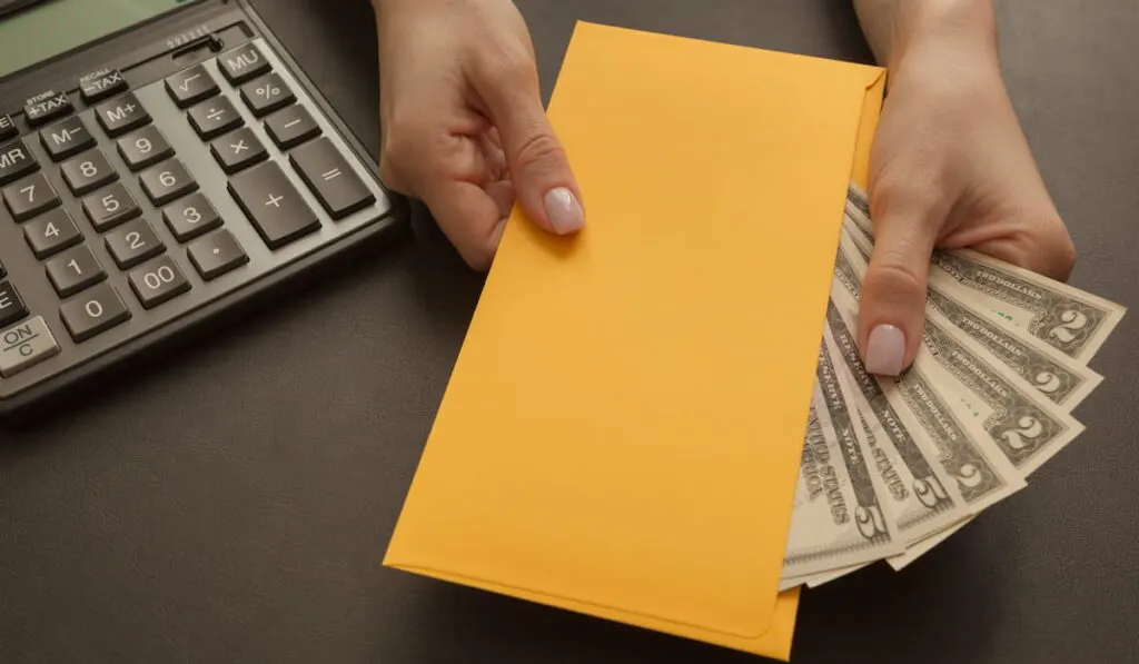 woman holding a yellow folder with money and a calculator on the table