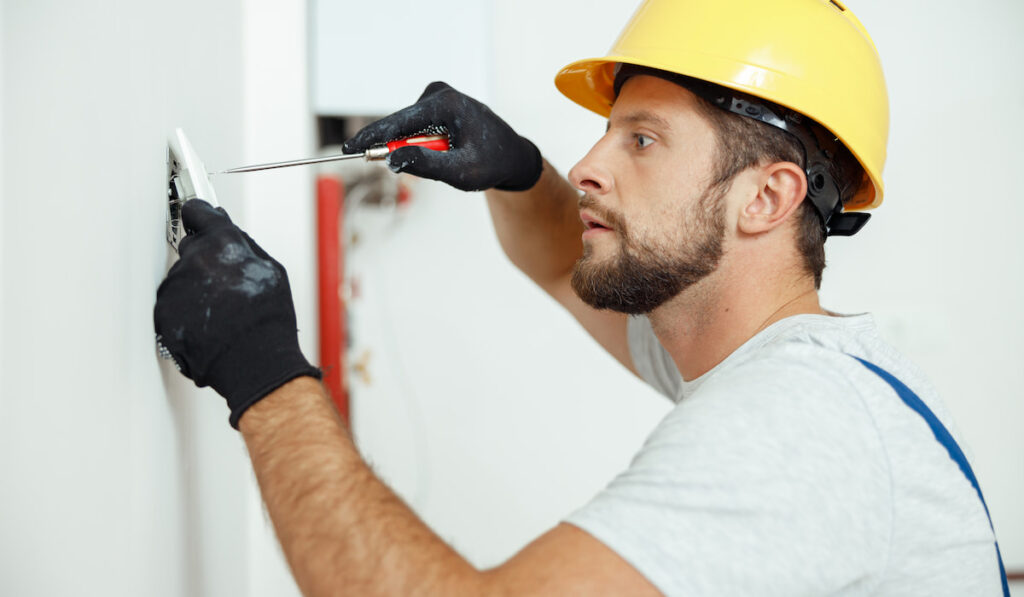 male worker professional electrician in uniform inspecting electrical outlet in apartment 