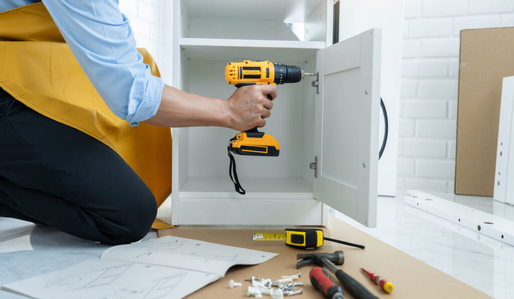 man holding cordless screwdriver drill and screws lie for screwing a screw assembling furniture at home