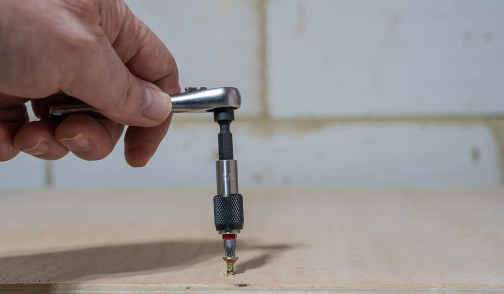 man tightening a brass screw into a plywood workbench using a quarter inch ratchet socket screwdriver with phillips bit