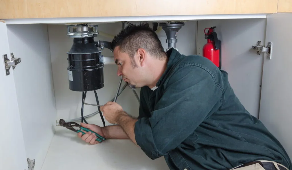 plumber laying under a house hold sink working on a garbage disposal.