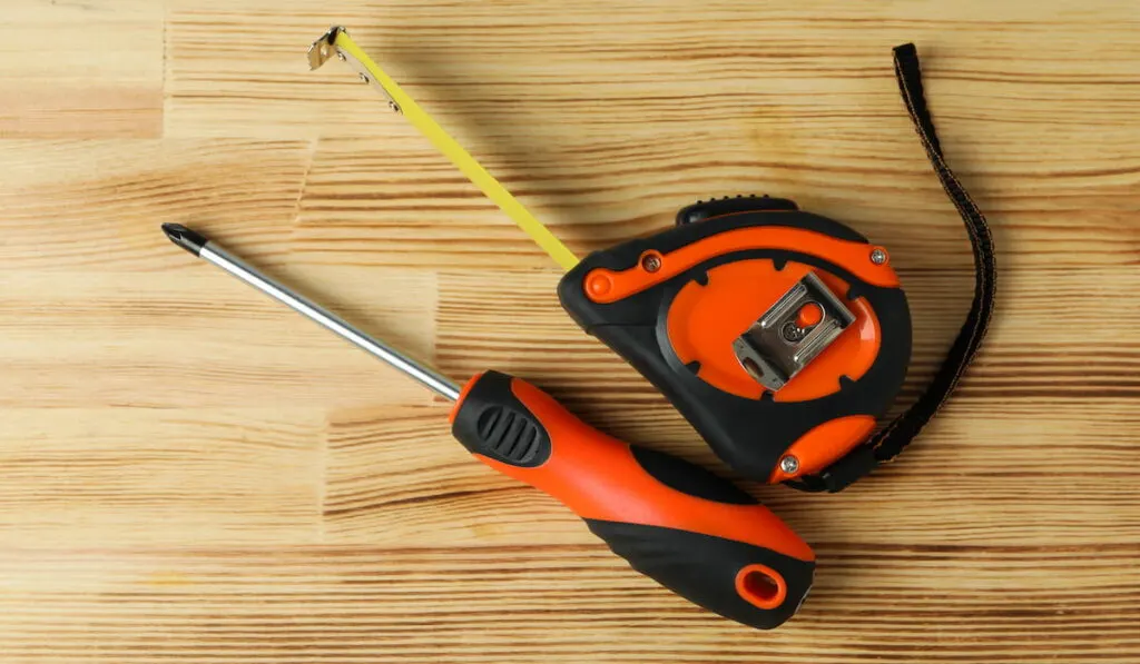 screwdriver and measure tape on wooden background