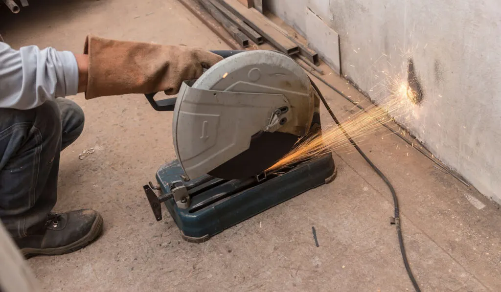 Using a chop saw on the floor to cut a piece of steel square tube. 