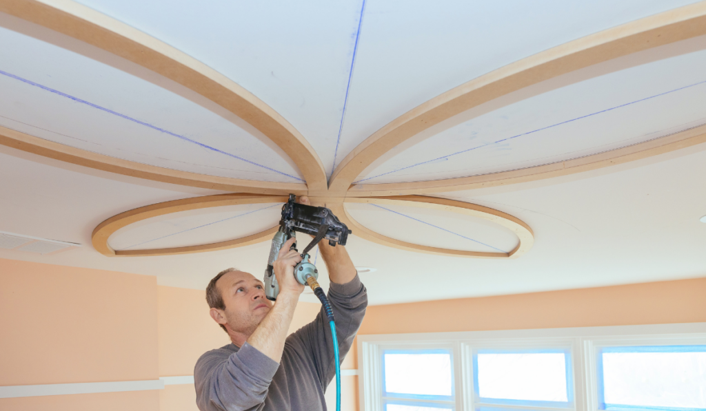 Carpenter using nail gun decorative unfinished molding on the ceiling
