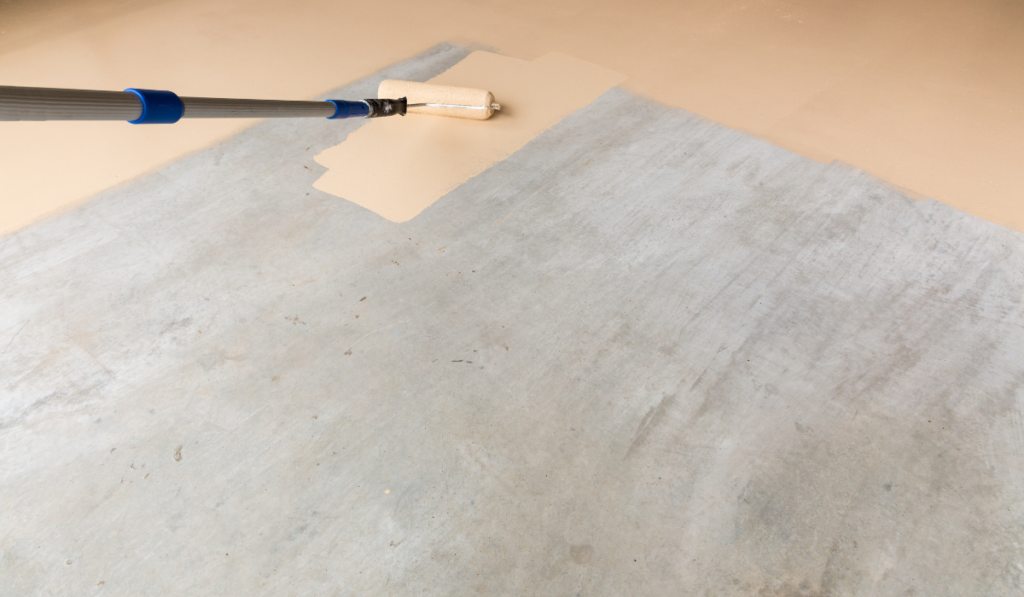 Worker Painting Floor of Garage with Roller.
