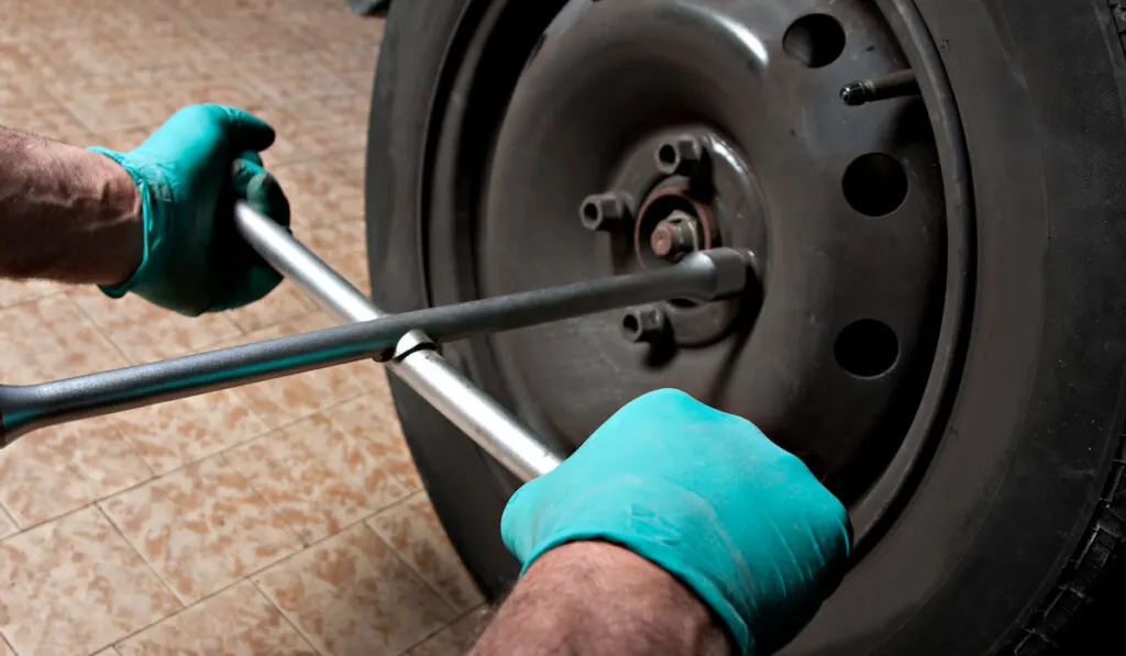 Car mechanic hand using lug wrench to uninstall the wheel nuts 