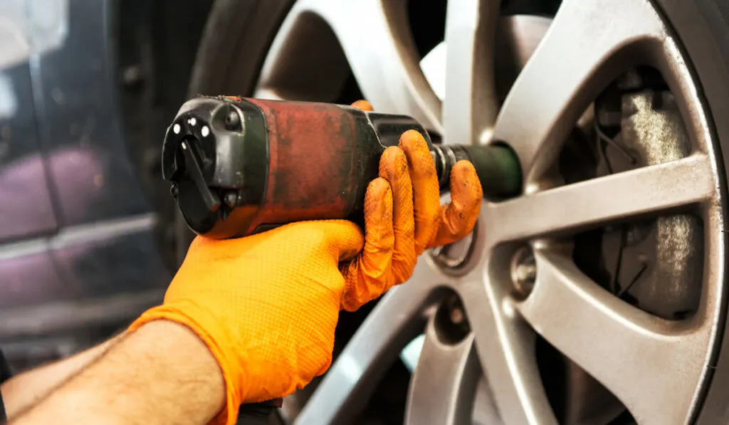 Closeup view of mechanic unscrewing car wheel with impact wrench