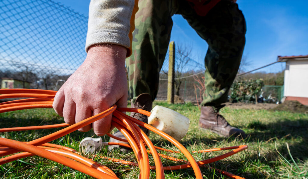 Gardener picking up an extension cord from the grass ground