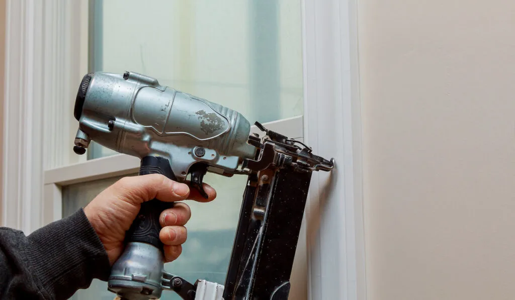 Man using a Finish nailer completing up a wall section of a house