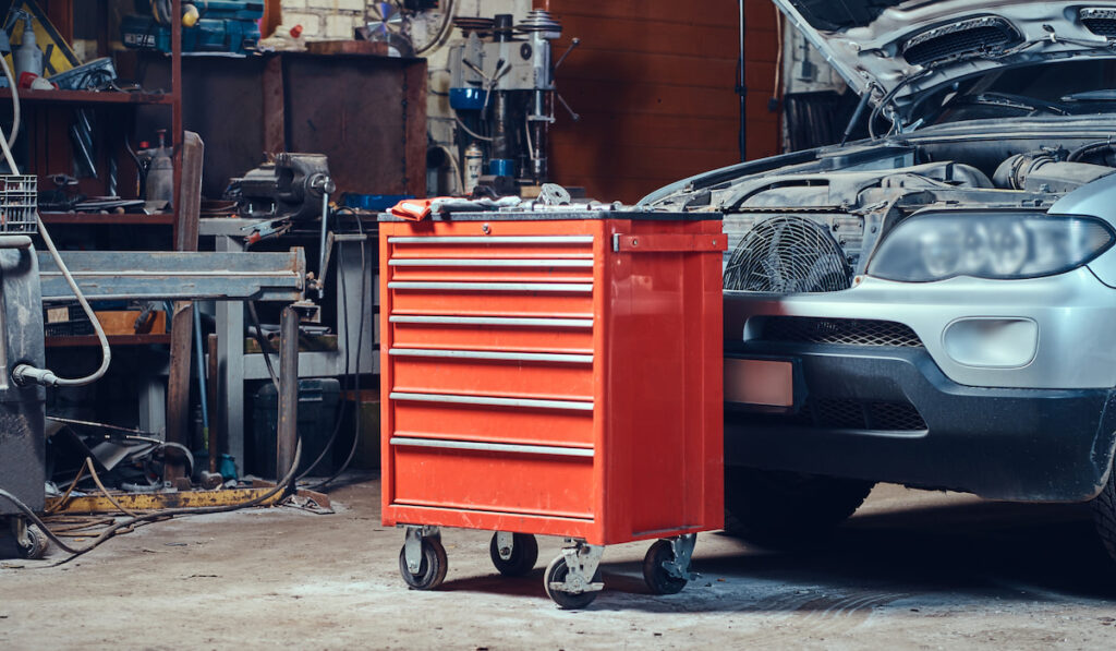 Red tool box in a garage with wheels near a car