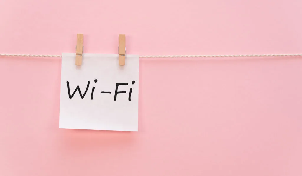 Wi-Fi inscription on a white paper hanging by a thread on a pink background