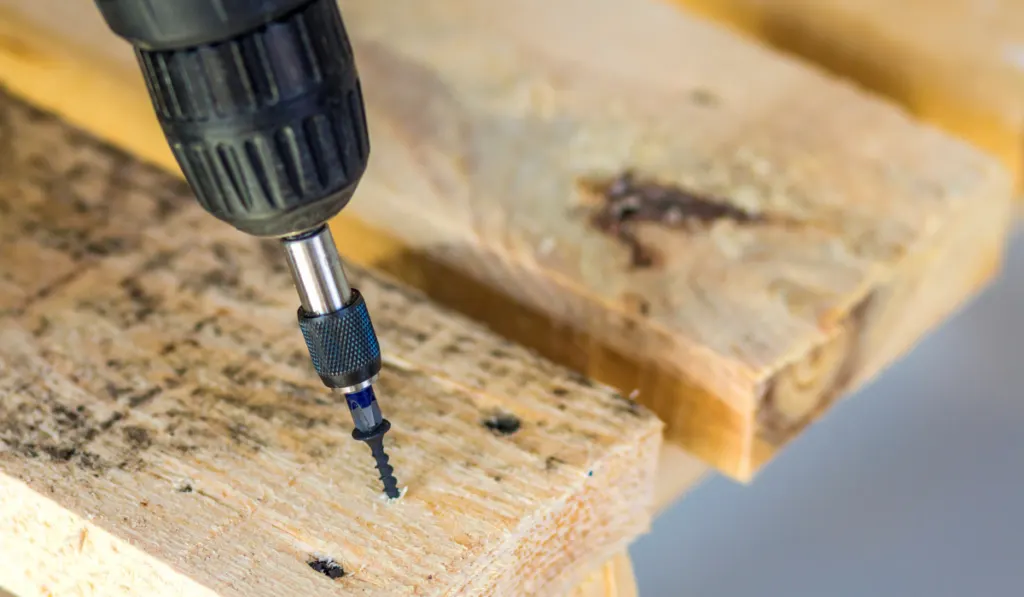 Workers hand with electric screwdriver screwing a screw into wooden board
