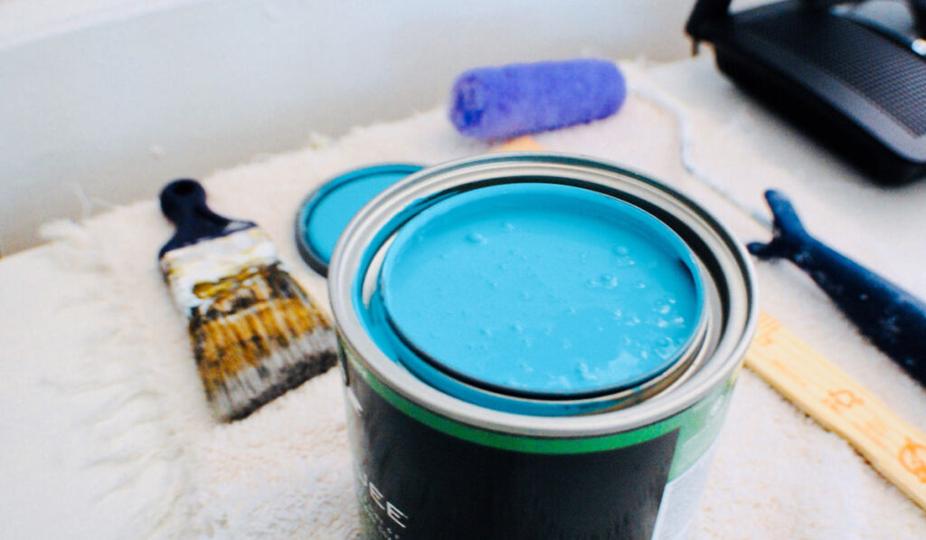 An opened can of turquoise paint and paintbrushes for painting 