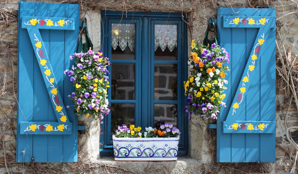 Flowering viola in a hand-painted folkloric flower pot on a window with a blue shutters
