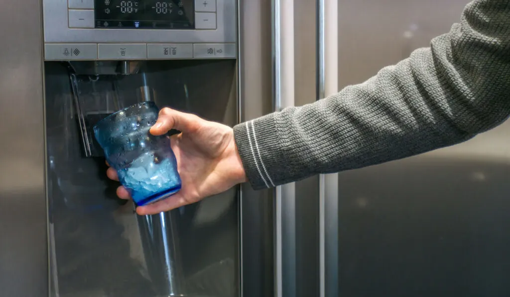 Male hand pouring cold water and ice cubes from home fridge