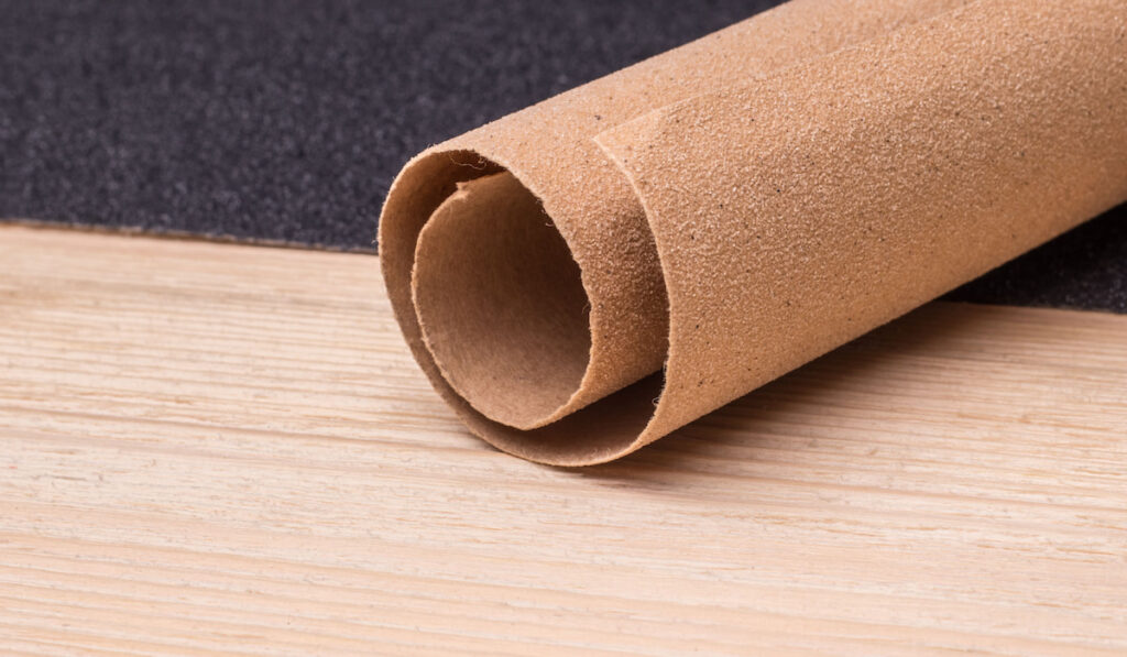 Roll and sheet of sandpaper on a laminate surface