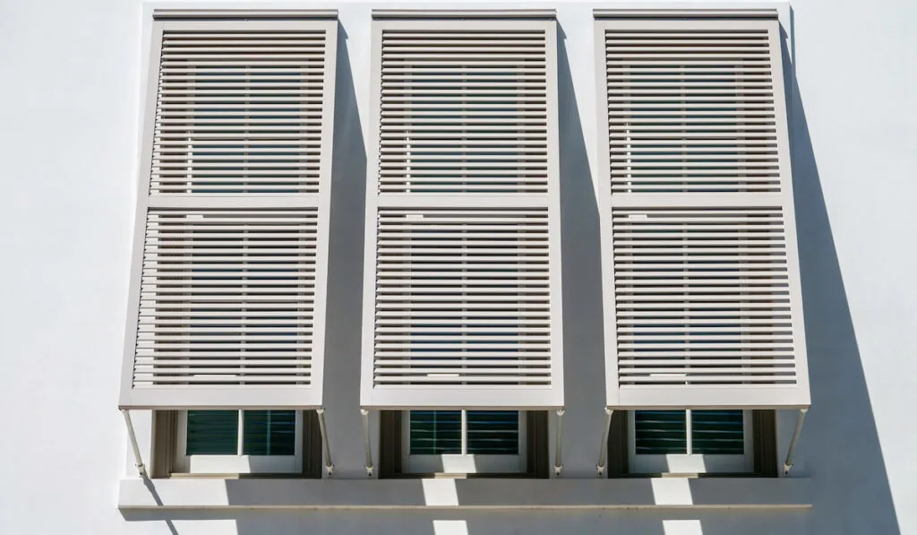 Three Bahama shutters also known as Bermuda Shutters on three windows of a building