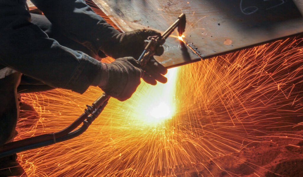 Worker using oxy-fuel torch cutting metal 