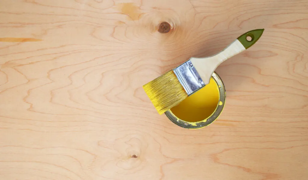 Yellow paint and a brush on a wooden background