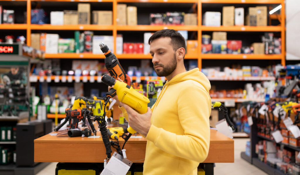 Young man compare two drills in a power tool store