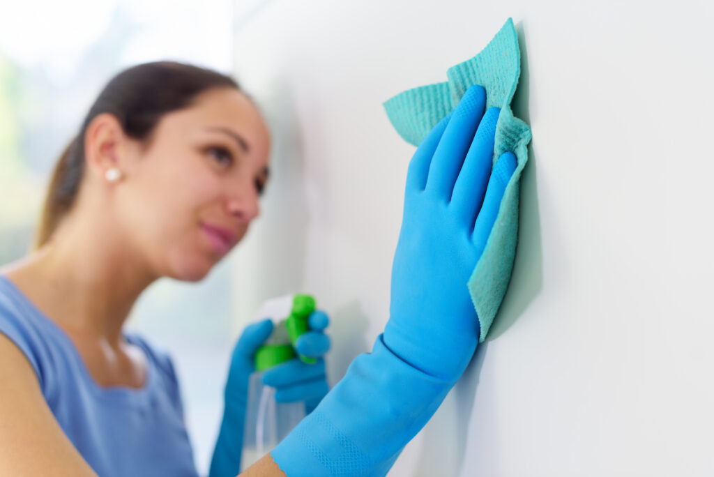 woman with ponytail cleaning wall surface with blue gloves and rug