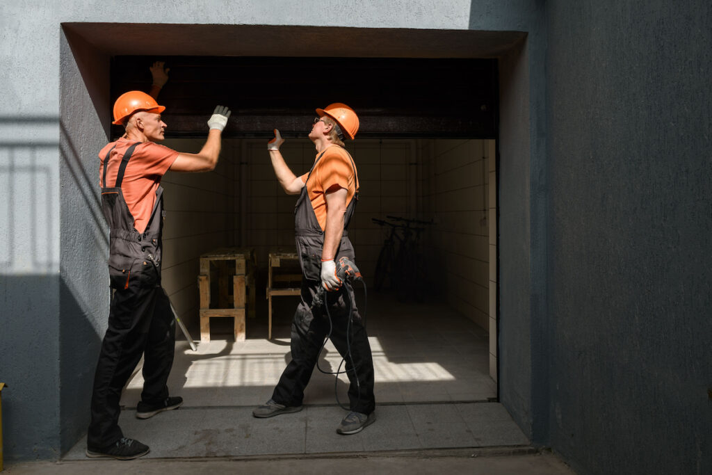 Two workers lifting gate in the garage fixing door garage