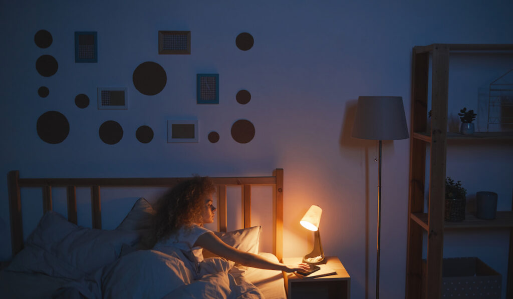 young woman lying in bed switching off lamp preparing to sleep